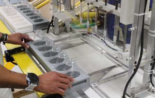 A tray of empty bottles is loaded into a liquid filling machine.