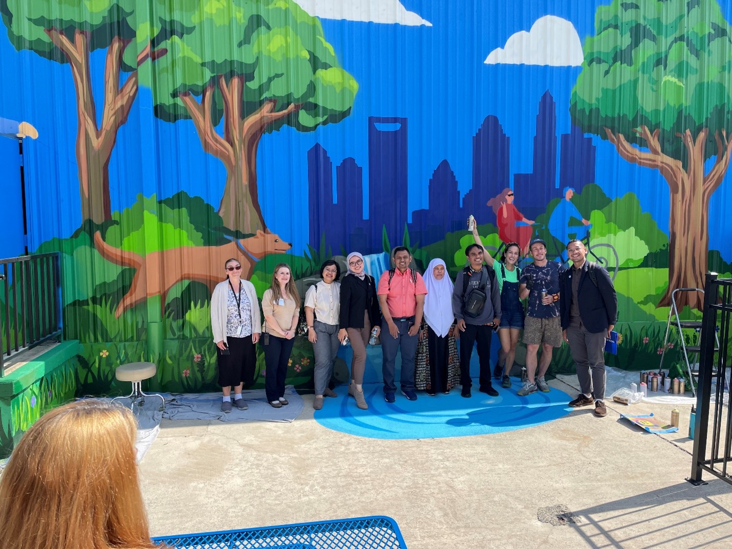 Picture consists of Delegates Standing in front of LSI Mural